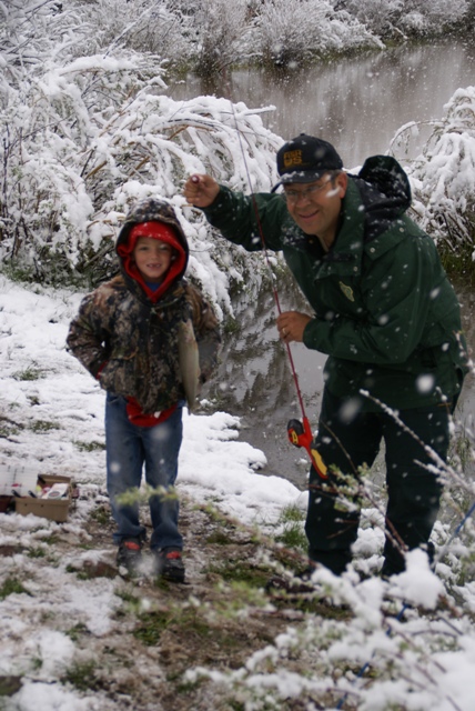 Photo of child and US Forest Service worker holding fish caught during a snowstorm in JUne as part of the annual Kid's Fishing Derby at the Moose Ponds